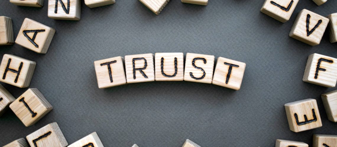 the word trust wooden cubes with burnt letters, trust in family relationships, gray background top view, scattered cubes around random letters